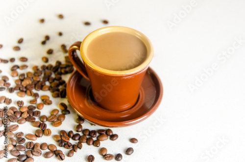 Old rare Scandinavian cup brown color of baked clay with coffee and milk in a saucer placed on a table on which coffee beans are scattered Arabica