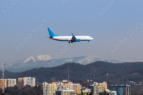 Passenger aircraft flies low over the city against the background of high snow-capped mountains