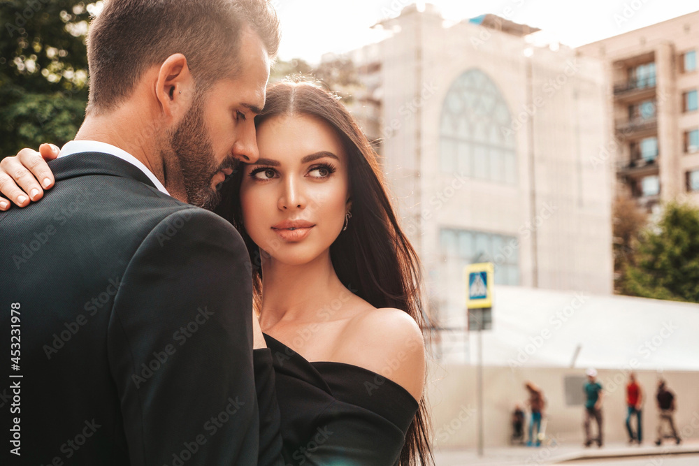 Beautiful fashion woman and her handsome elegant boyfriend in suit. Sexy brunette model in black evening dress. Fashionable couple posing in the street in Europe. Brutal man and his female outdoors Beautiful fashion woman and her handsome elegant boyfriend in suit. Sexy brunette model in black evening dress. Fashionable couple posing in the street in Europe. Brutal man and his female outdoors