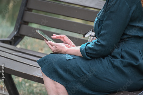 In the hands of a mature woman holding a smartphone, the woman sits on a park bench and exchanging messages online.