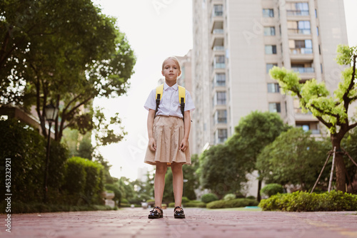 Schoolgirl back to school after summer vacations. Child in uniform smiling early morning outdoor. 