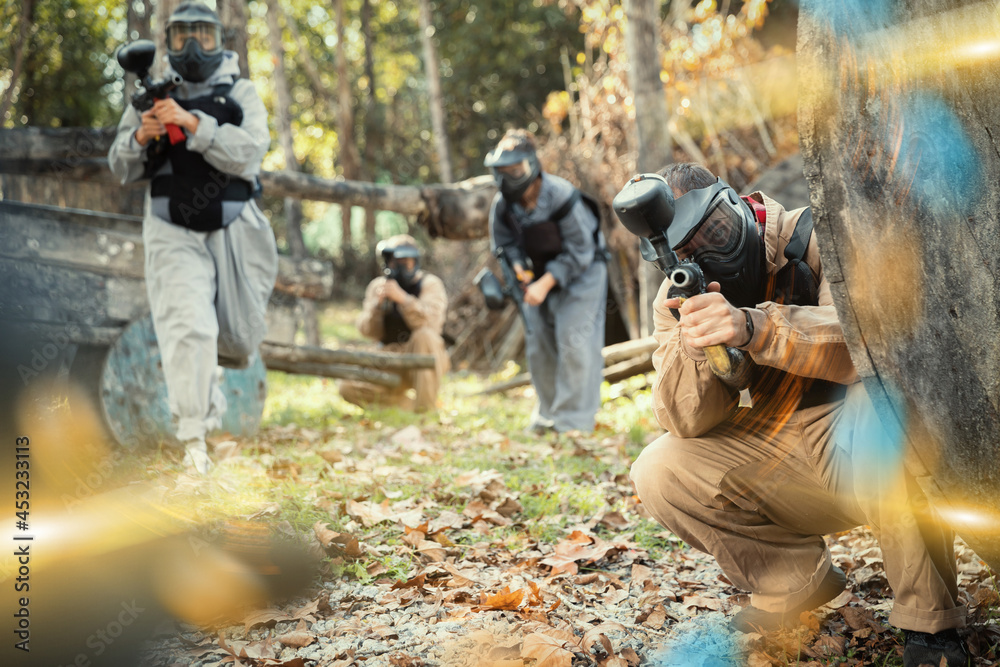 Fototapeta premium Men and women in protective uniform playing paintball on shooting range