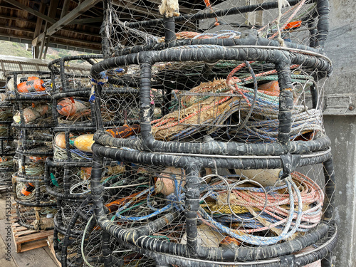 Large, old, round crab traps stacked in wharf warehouse with ropes and buoys inside