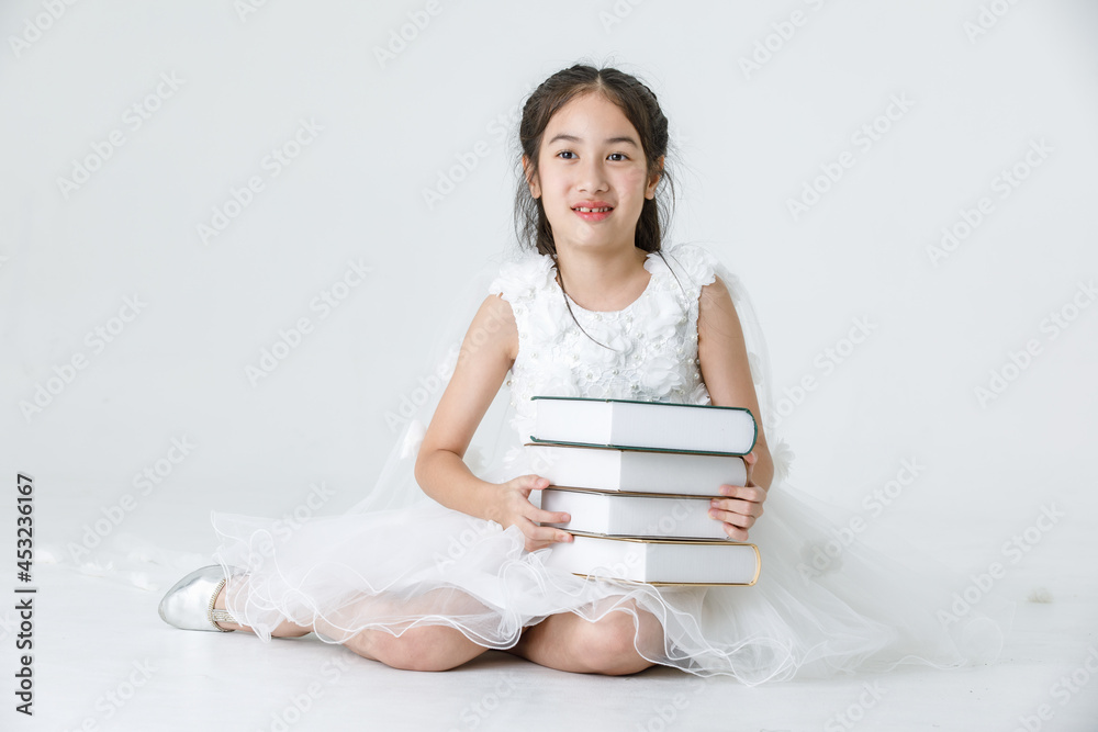 Portrait studio shot of Asian pretty girl wears white princess long rose flower dress fashion costume posing with stack of books on white background Portrait studio shot of Asian pretty girl wears white princess long rose flower dress fashion costume posing with stack of books on white background
