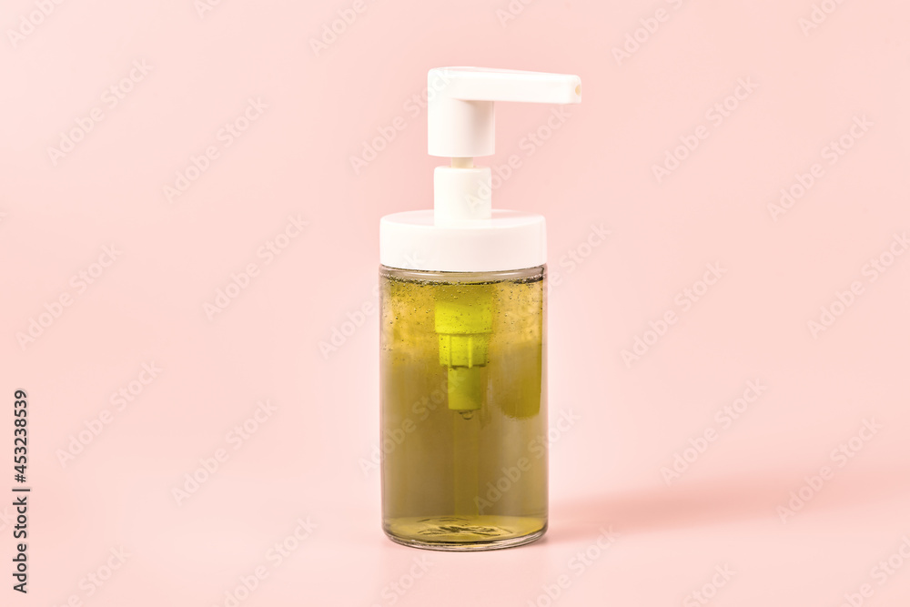 transparent dispenser with green liquid soap on a pink background, close-up. shower gel. minimalistic cosmetic concept