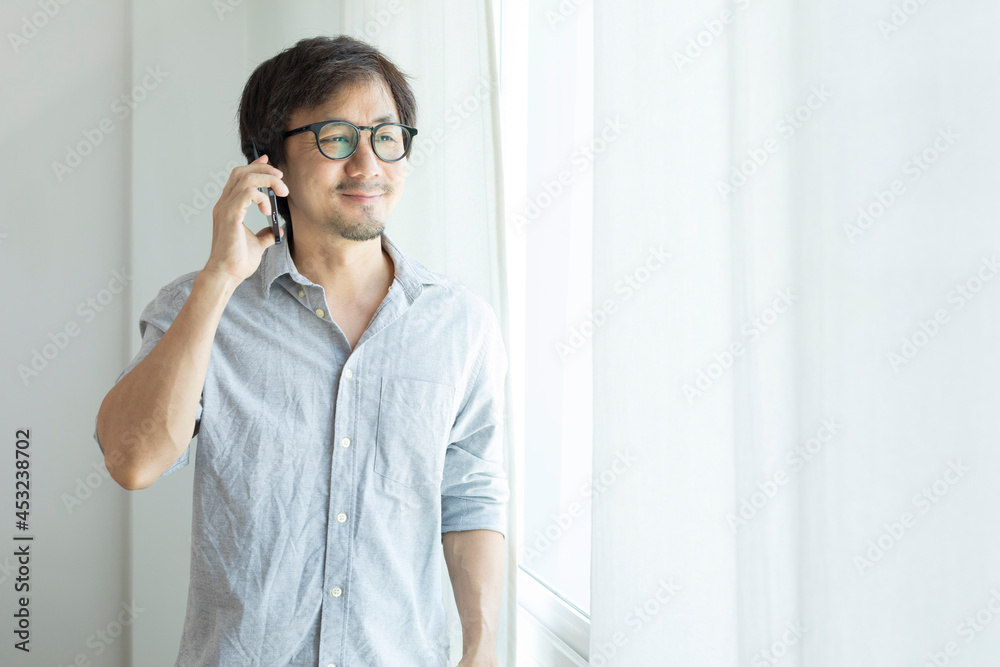 Asian businessman texting on smartphone standing next to window. Asian businessman texting on smartphone standing next to window.