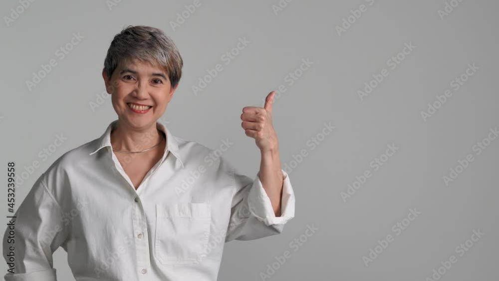 Middle aged Asian woman pointing fingers up at empty copy space for text isolated on white background