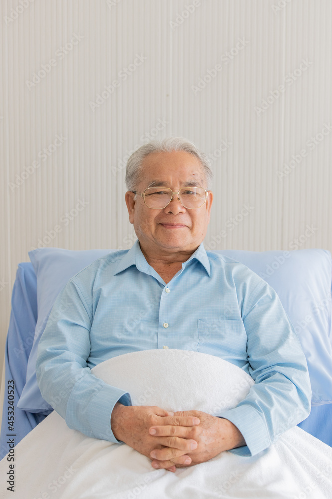 Close up portrait shot of an old fat asian patient with gray hair wearing eyeglasses and light blue long sleeve shirt sitting on hospital bed cover his lower body with white clean blanket Close up portrait shot of an old fat asian patient with gray hair wearing eyeglasses and light blue long sleeve shirt sitting on hospital bed cover his lower body with white clean blanket