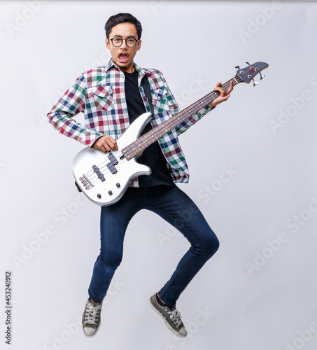 Portrait shot of young teenage musician playing the bass guitar with emotion in the studio. Professional young junior bassist holding bass guitar and looking at camera isolated with white background