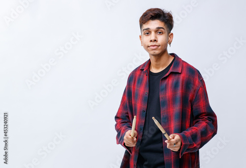 Portrait shot of an attractive young teenage musician holding drumsticks in the studio. Young trendy junior drummer looking and pointing the drumsticks to the camera isolated with white background photo