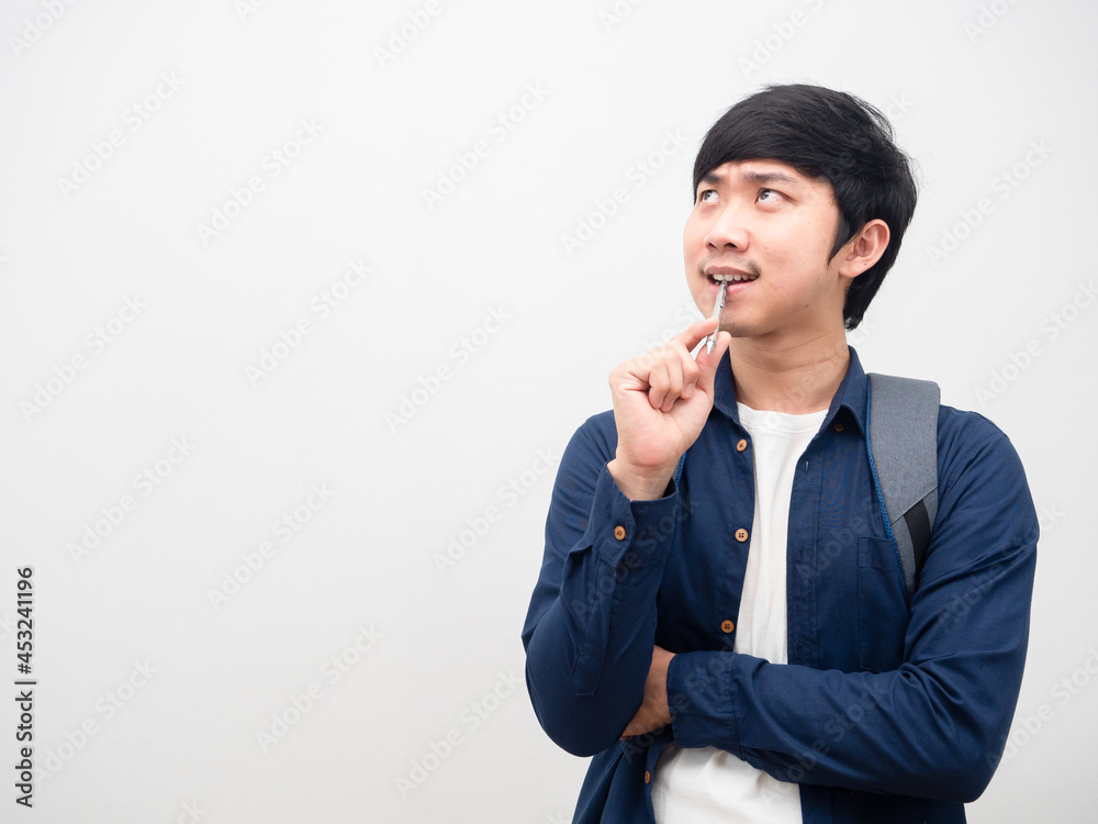 Asian man with backpack bite pen serious face thinking something look at space white background Asian man with backpack bite pen serious face thinking something look at space white background