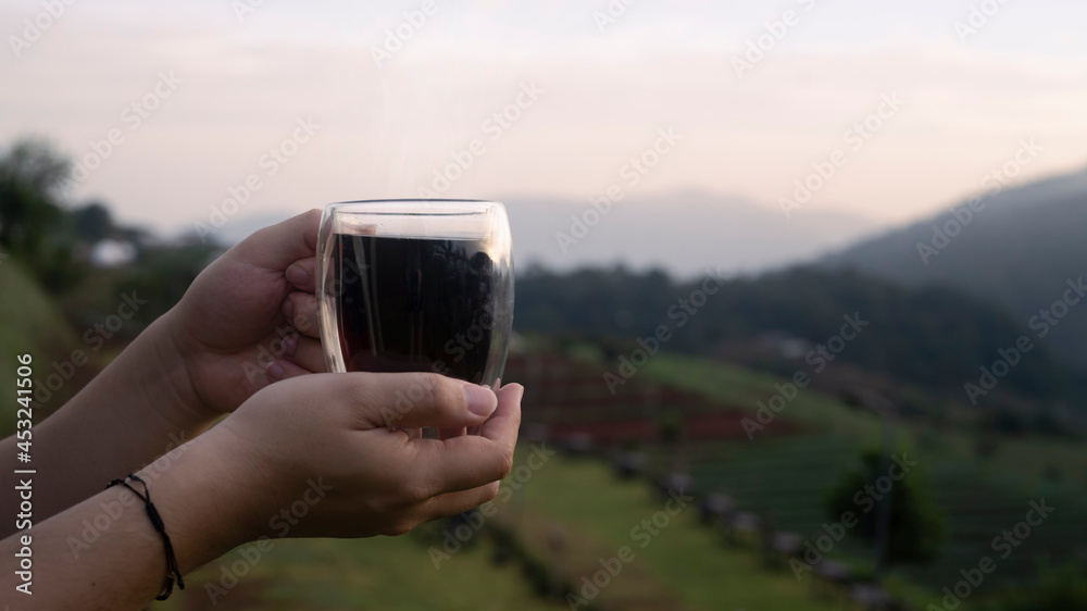 Man holding coffee cup with blurred natural mountain view in background.