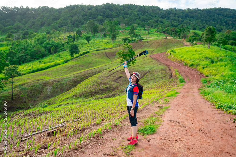 Asian female trail runner wearing sportswear is taking a portrait with a view of a high mountain running track in a dirt road on a clear day, with a mountain view in the background.