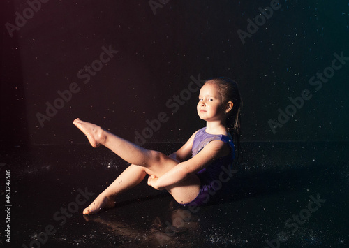 a little charming cute girl gymnast in the water on a black background in the aqua studio does sports exercises. kontsepkija sprotivnfh goods, advertising for the shopping center