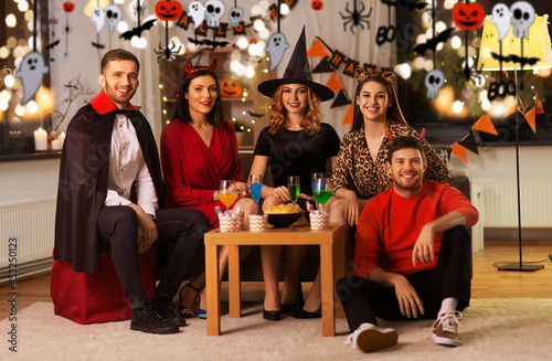 friendship, holiday and people concept - group of happy smiling friends in halloween costumes of vampire, devil, witch and cheetah at home party at night