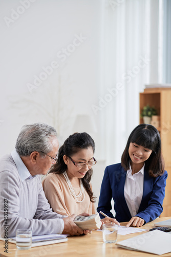 Smiling real estate agent asking senior couple to sign document after they pay deposit for house