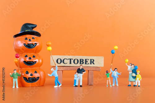 Miniature people Happy family with pumpkin on orange background, Hello October concept 