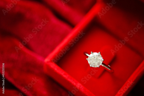 Diamond ring in jewelry gift box on red fabric background