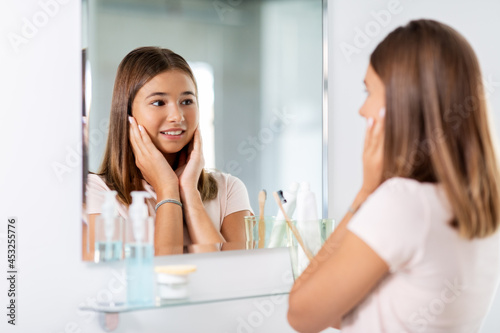 beauty, hygiene and people concept - teenage girl looking in mirror at bathroom