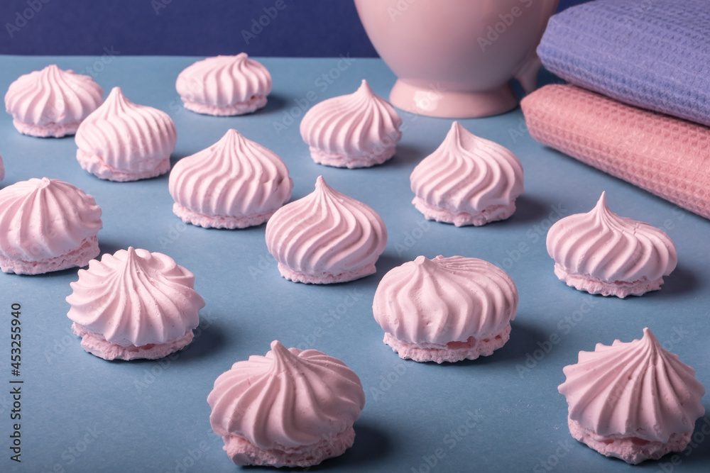 Beautifully arranged rows of delicate pink meringue cookies on a light blue background next to a harmonious pink and blue cloth napkins and a pink large cup. Light dessert. Beautifully arranged rows of delicate pink meringue cookies on a light blue background next to a harmonious pink and blue cloth napkins and a pink large cup. Light dessert.