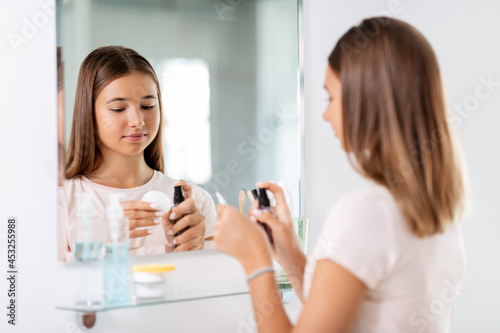 beauty  hygiene and people concept - teenage girl applying lotion to cotton disc at bathroom