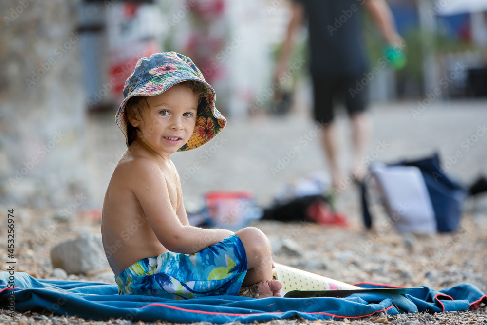 Cute blond toddler boy, reading a book on the beach Cute blond toddler boy, reading a book on the beach
