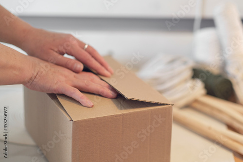 woman entrepreneur packs a handmade product in a cardboard box. delivery of goods for a small business. an elderly woman earns her hobby from home. © yavdat