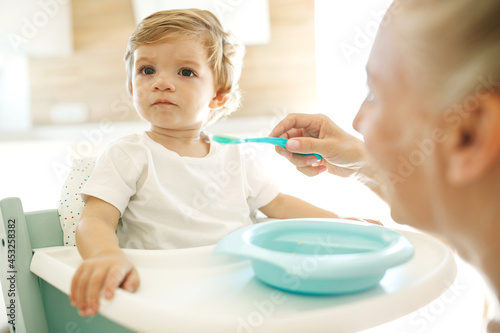 Mom feeds the baby. Young woman feeds her baby from a spoon at home. High quality photo.