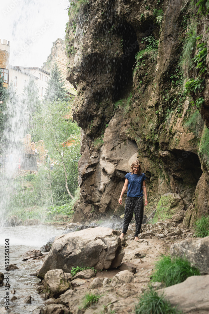 Woman walking by beautiful mountain waterfall