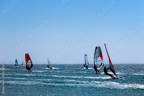 Kefalos beach, Gokceada, Turkey - 21-08-2021 colorful windsurfers on a windy day. Practicing wind surfing. People are engaged in sailing, windsurfing.