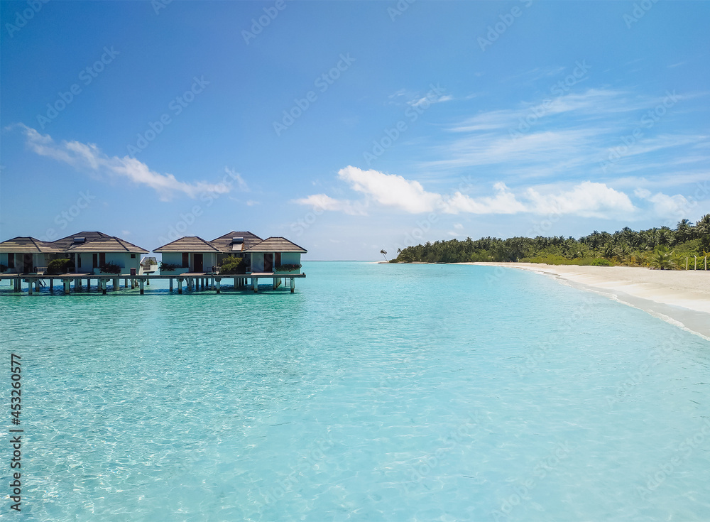 View of water villas (bungalows) near the island in the Maldives, surrounded by the beautiful transparent turquoise Indian Ocean. The concept of an exotic summer vacation, resort.