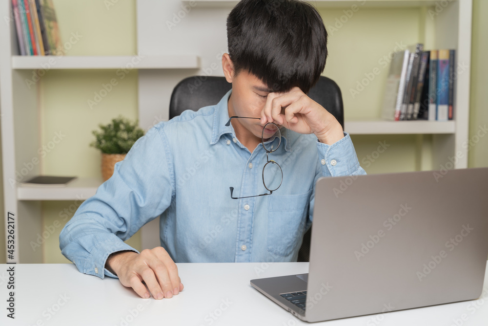 Stressed tired young Asian man in business shirt touch eyes from bad vision sight in pain eyestrain, holding glasses when eyes fatigued from overworked, laptop computer work at home. Tired man concept Stressed tired young Asian man in business shirt touch eyes from bad vision sight in pain eyestrain, holding glasses when eyes fatigued from overworked, laptop computer work at home. Tired man concept