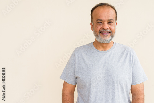 Portrait of happy bearded Indian man smiling against plain wall