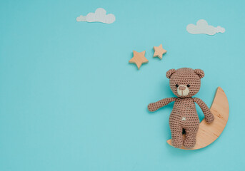 Kids toy knitted soft bear with wooden moon and stars on blue background