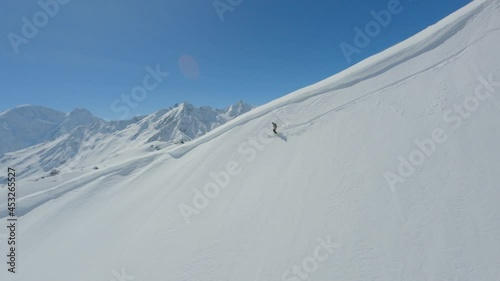 Aerial follow view active freerider riding skiing on top ridge downhill high natural mountain with snow field enjoy extreme sport activity. Flying fpv drone performing trick jumping at ski resort