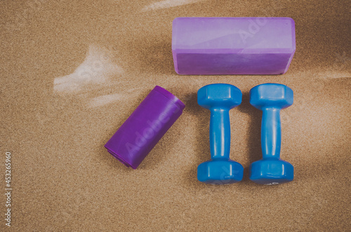 Flat lay of 3kg blue dumbbells, purple resistance band and purple block on a cork yoga mat. Concept: workout objects for home fitness practice photo