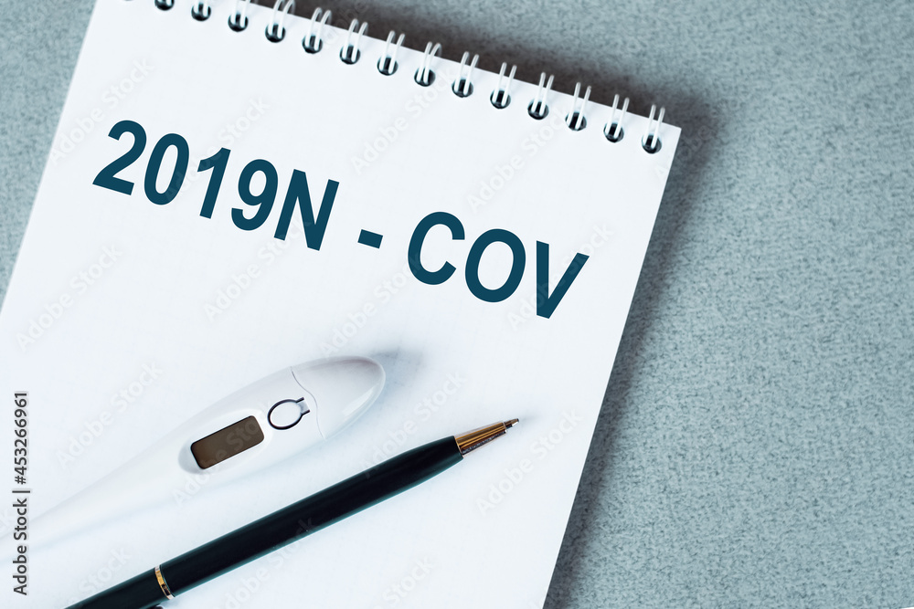 Blank notebook with thermometre and pen on table. 2019n - COV text.