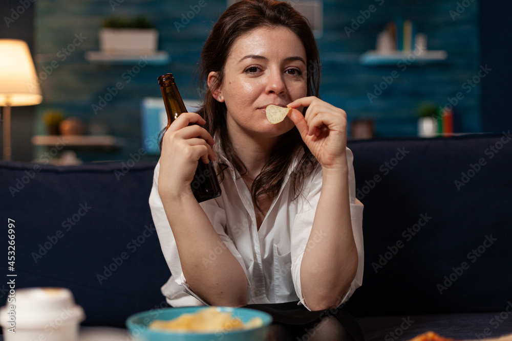 Portrait of woman looking into camera eating tasty delicious snack enjoying takeaway food home delivered. Caucasian female relaxing on sofa late at night in living room. Fastfood lunch meal order Portrait of woman looking into camera eating tasty delicious snack enjoying takeaway food home delivered. Caucasian female relaxing on sofa late at night in living room. Fastfood lunch meal order