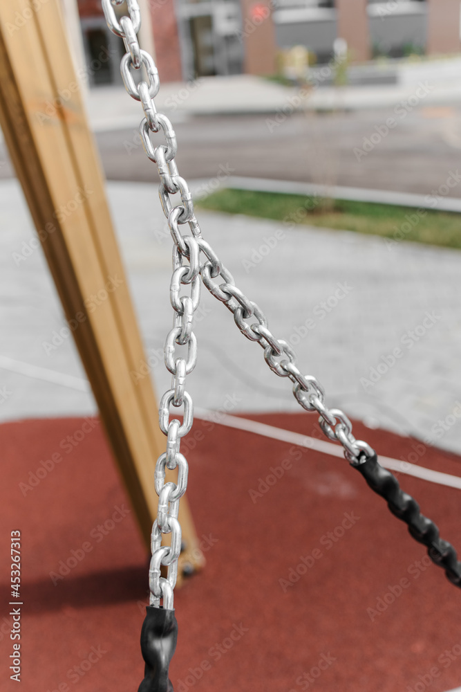 An element of a children's swing. rubberized metal chain. A summer day. Outdoor colorful Playground with rubber flooring next to the house. An element of a children's swing. rubberized metal chain. A summer day. Outdoor colorful Playground with rubber flooring next to the house.