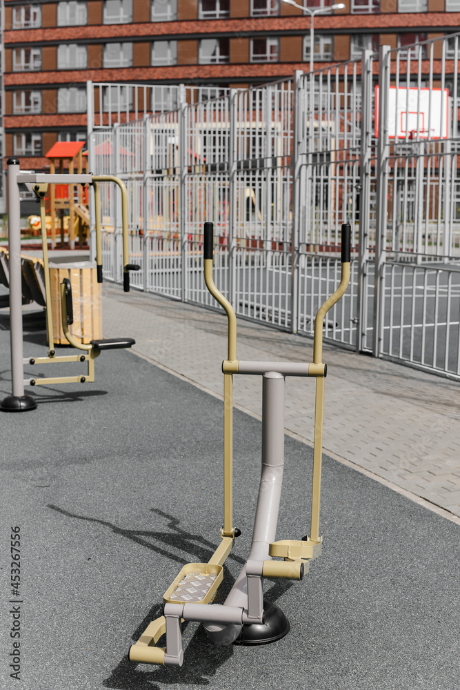 Metal exercise machines on a street platform. An outdoor sports ground with exercise equipment near the house. A summer day.