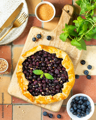 French galette or pie with blueberry on a wooden serving board on a culinary background top view. Summer homemade sweet pastries	