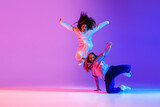 Two active young girls dancing hip-hop on gradient pink purple neon studio background