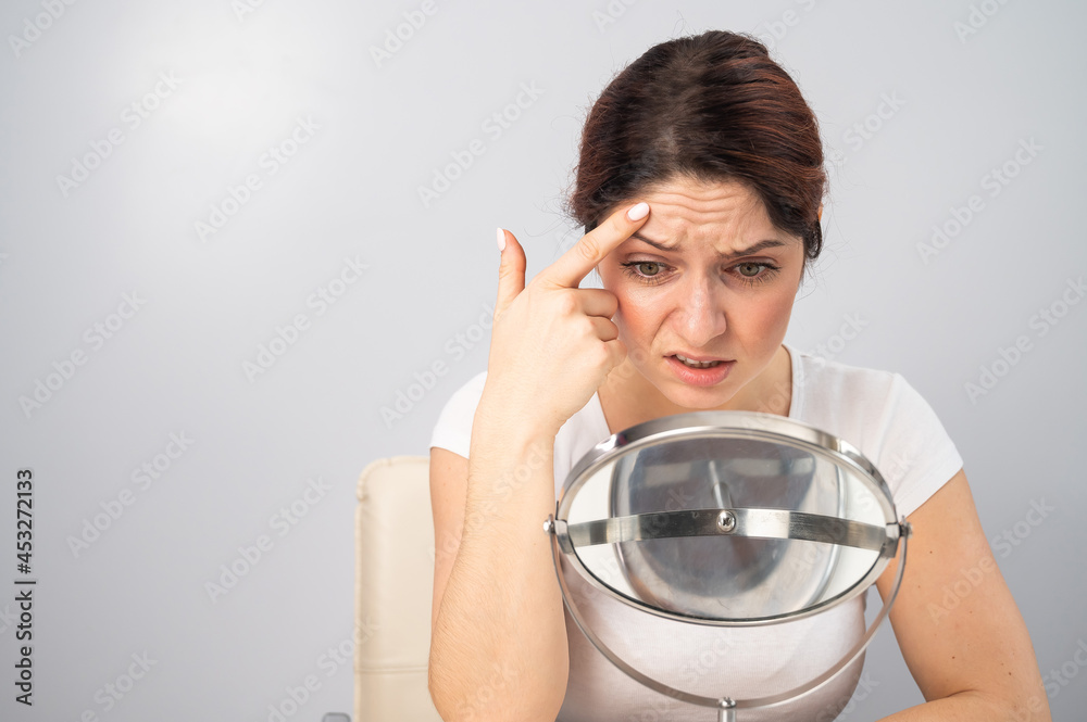 Caucasian woman looks at herself in the mirror and is upset because of facial wrinkles on her face. Caucasian woman looks at herself in the mirror and is upset because of facial wrinkles on her face.