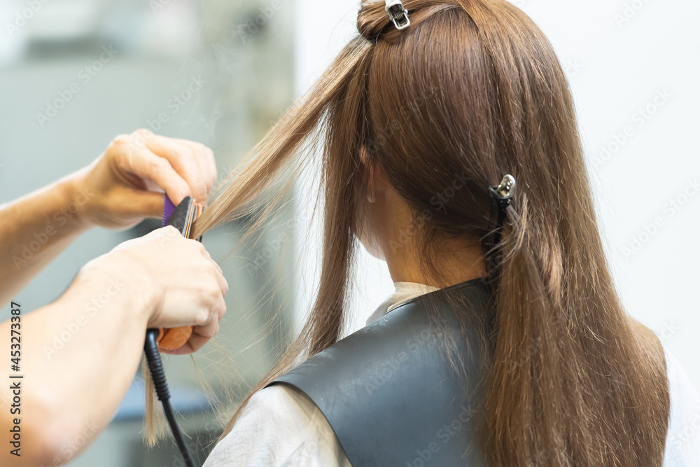 Fototapeta premium ヘアアイロンを使ってセットするスタイリスト