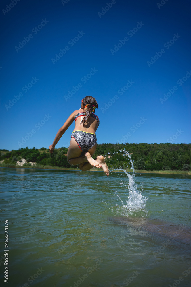 Fototapeta premium A little cute girl in a swimsuit jumps into the blue water of a career lake.