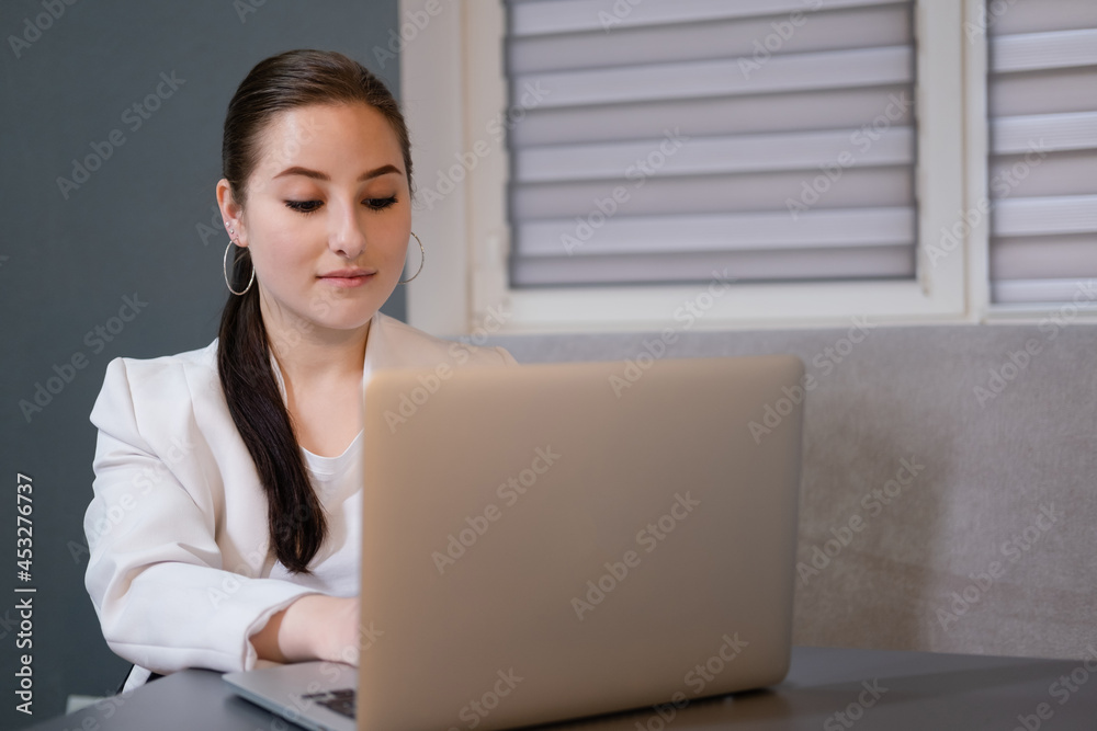 brunette woman use laptop in grey room. freelancer. working from home. student, remote study brunette woman use laptop in grey room. freelancer. working from home. student, remote study