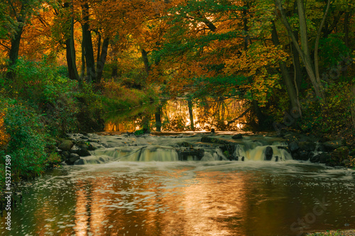 Wodospad na małej rzece w jesienny wieczór. Światło zachodzącego słońca nadaje wodzie czerwone zabarwienie.