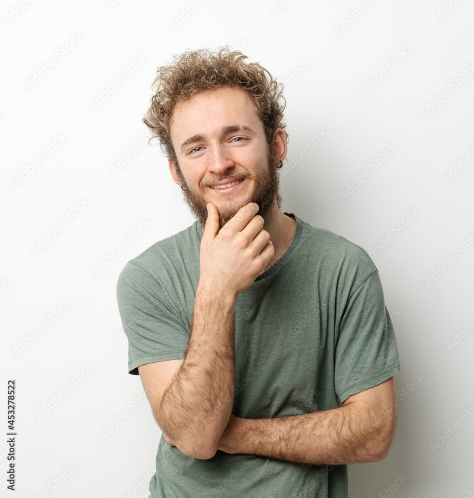 Curly hair smiling handsome young man looking at camera touching chin dressed in olive t-shirt isolated on white background. Portrait of smiling young man with hands folded. Curly hair smiling handsome young man looking at camera touching chin dressed in olive t-shirt isolated on white background. Portrait of smiling young man with hands folded.