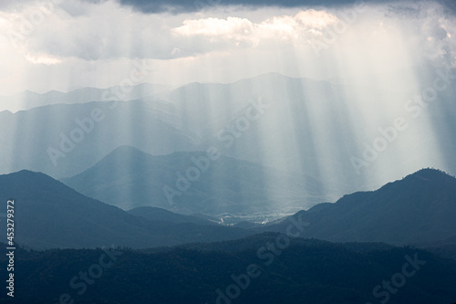 Dramatic sunlight from cloudy sky shining to dark blue mountain range.