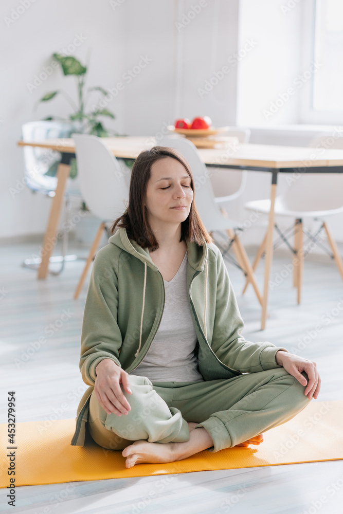 meditation and yoga at home, beautiful and young European woman doing yoga and breathing practices in her home. woman sitting in lotus pose with eyes closed, green suit for sports, beautiful cozy meditation and yoga at home, beautiful and young European woman doing yoga and breathing practices in her home. woman sitting in lotus pose with eyes closed, green suit for sports, beautiful cozy